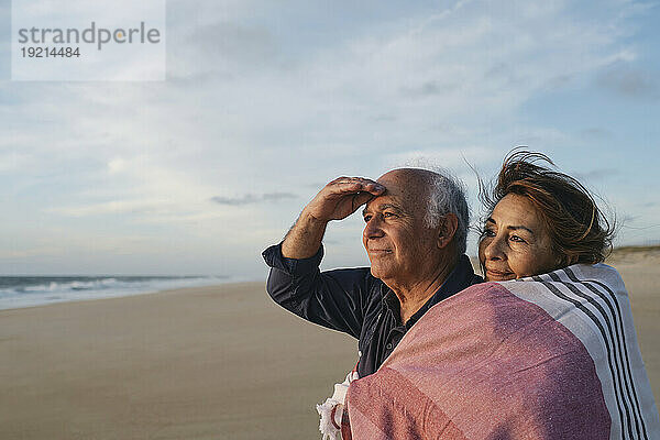 Lächelnder älterer Mann und Frau in Schal gehüllt am Strand