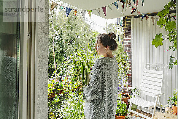 Teenage girl holding potted plant standing on balcony at home