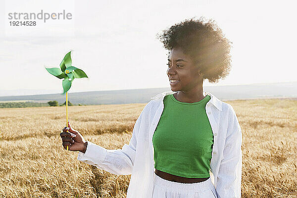 Smiling afro woman holding pinhwheel toy in field