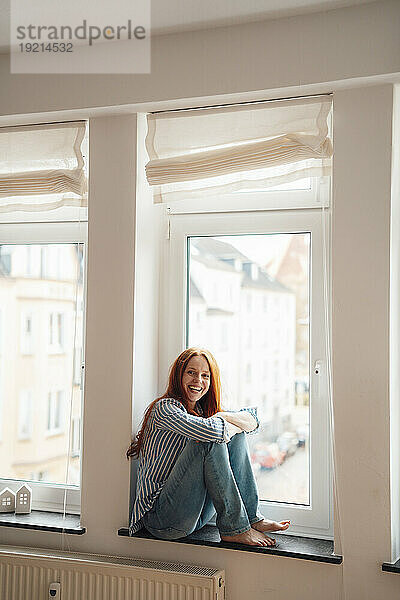 Glückliche Frau sitzt zu Hause auf der Fensterbank