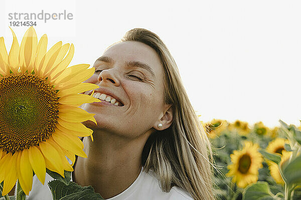 Frau mit geschlossenen Augen lacht im Sonnenblumenfeld