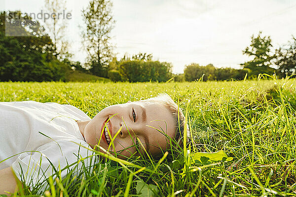 Lächelnder Junge liegt im Gras im Park