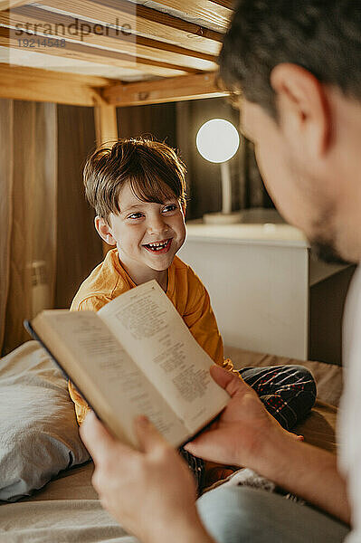 Father reading book to happy son in bunk bed at home