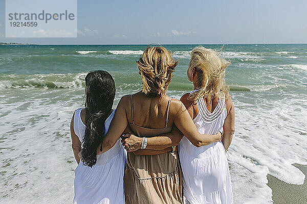 Friends looking at sea standing with arms around on shore