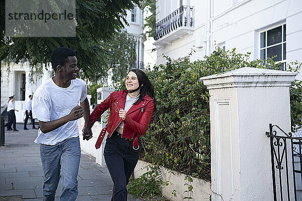 Fröhliches junges Paar hält Händchen und rennt in die Nähe des Gebäudes