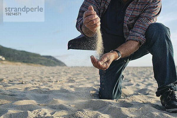 Älterer Mann hält Sand in der Hand am Strand