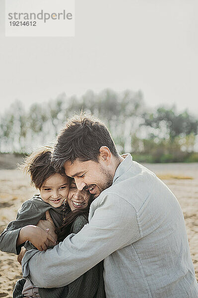 Liebevolle Eltern umarmen und umarmen ihren Sohn am Strand