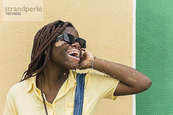 Glückliche junge Frau mit Sonnenbrille steht vor der Wand