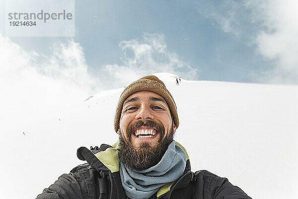 Glücklicher Mann mit Strickmütze macht ein Selfie im Schnee