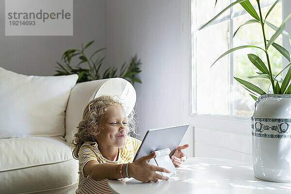 Blondes Mädchen schaut zu Hause auf den Tablet-PC auf dem Tisch