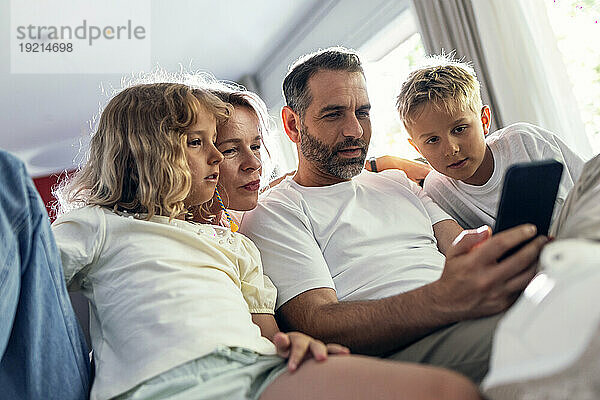 Vater teilt Mobiltelefon mit Familie  die im Wohnzimmer sitzt