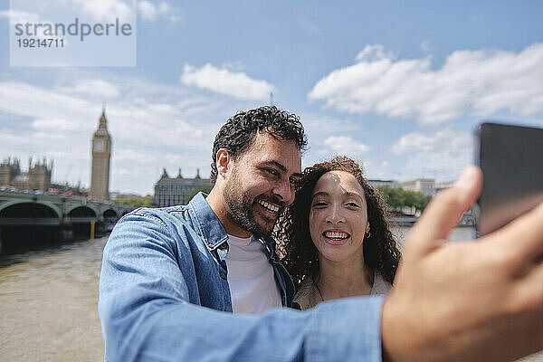 Lächelndes Paar macht Selfie unter bewölktem Himmel in der Stadt