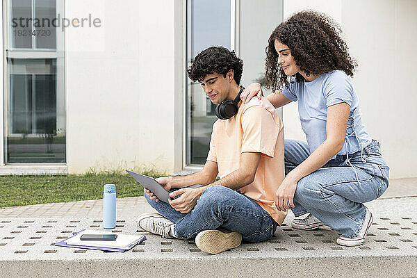 Lächelnde Studenten benutzen Laptop auf Betonbank auf dem Campus