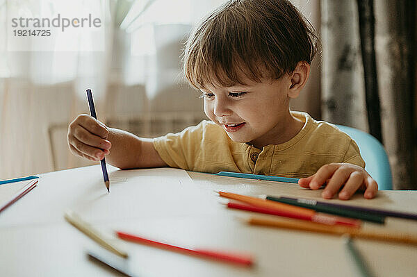 Smiling boy drawing with colored pencil at home
