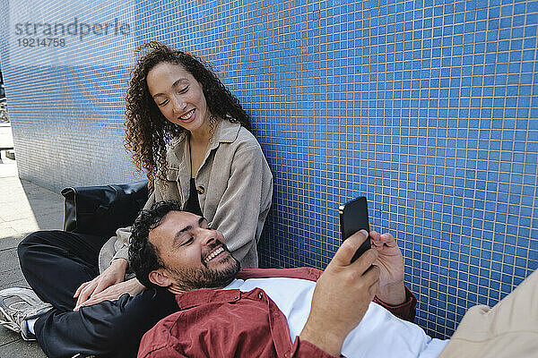 Glückliche Frau mit Mann entspannt sich und benutzt Smartphone in der Nähe der Wand