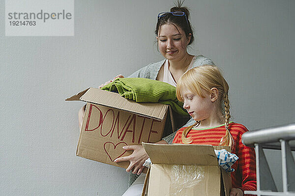Sisters with donation clothes in cardboard boxes by wall