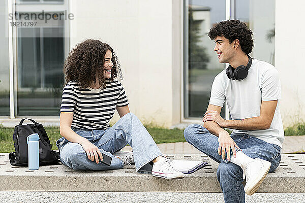 Glückliche Studenten sitzen auf einer Betonbank und lachen auf dem Campus