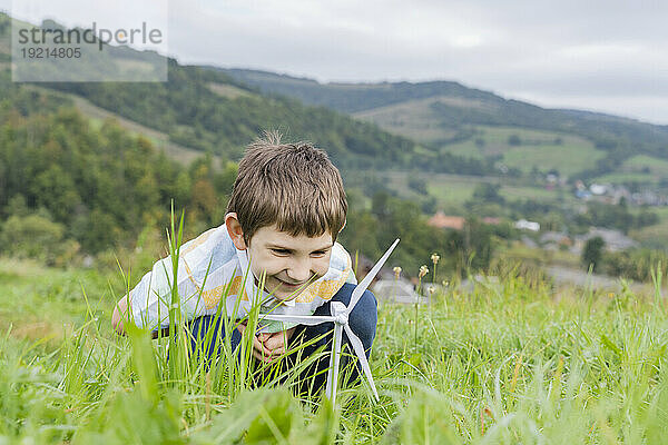 Lächelnder Junge blickt auf das Windturbinenmodell auf der Wiese