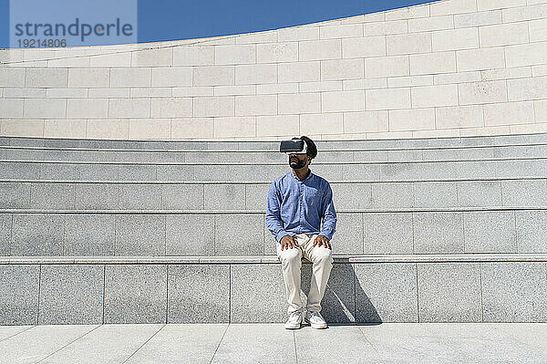 Junger Mann mit Virtual-Reality-Simulator sitzt auf der Treppe