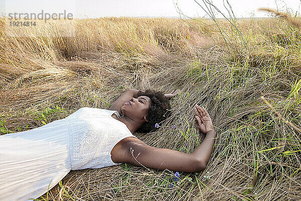 Frau mit geschlossenen Augen entspannt sich auf trockenem Gras im Feld