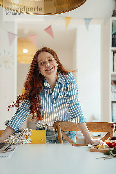 Lächelnde Frau lehnt zu Hause am Esstisch
