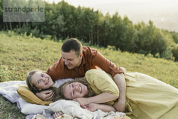 Lächelnde Familie  die Spaß daran hat  auf einer Decke auf der Wiese zu liegen