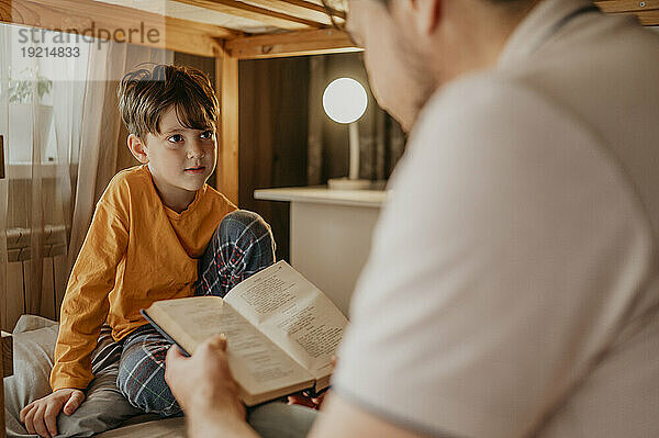 Vater liest seinem Sohn zu Hause im Etagenbett ein Buch vor