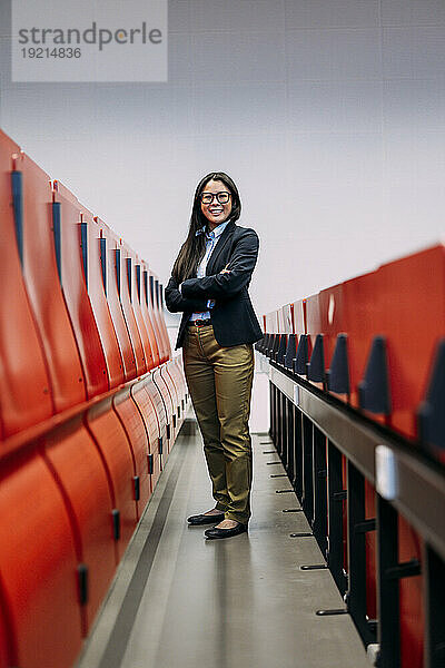Smiling businesswoman with arms crossed standing amidst red seats at convention center