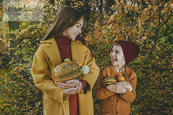 Smiling friends holding pumpkins in garden
