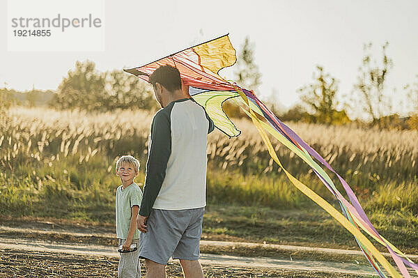 Vater und Sohn laufen mit buntem Drachen auf der Wiese