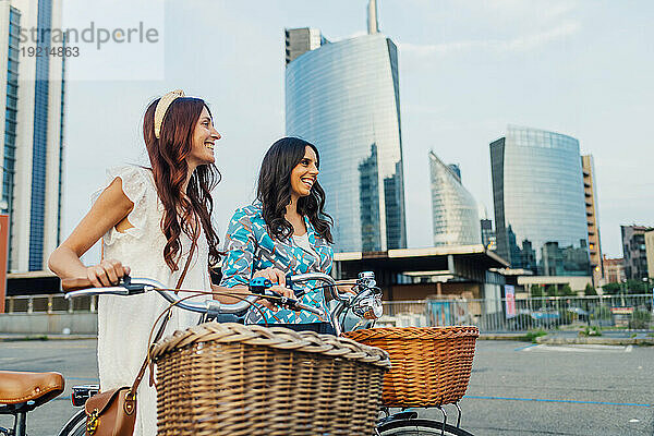 Happy friends with bicycles on road in front of buildings