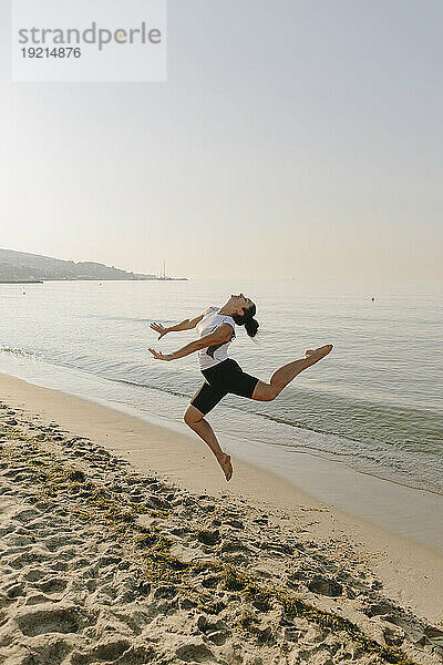 Frau springt am Strand vor das Meer