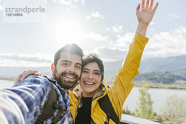 Glücklicher Mann  der mit erhobener Hand ein Selfie mit einer Frau macht