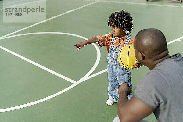 Vater und Junge halten Basketball in der Hand und gestikulieren auf dem Sportplatz