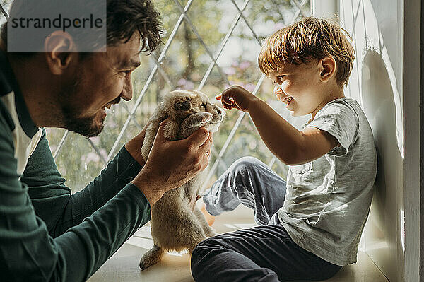 Happy father holding puppy in front of boy at home