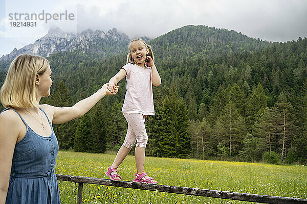 Frau hält Tochter an der Hand und geht auf Geländer vor Bergen