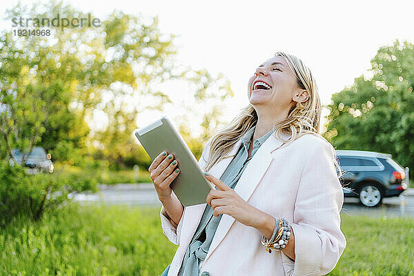 Glückliche Geschäftsfrau mit Tablet-PC lacht im Büropark
