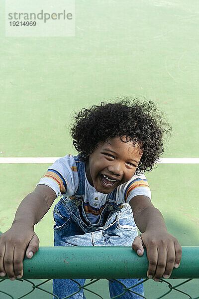 Lächelnder Junge hält Zaun am Sportplatz