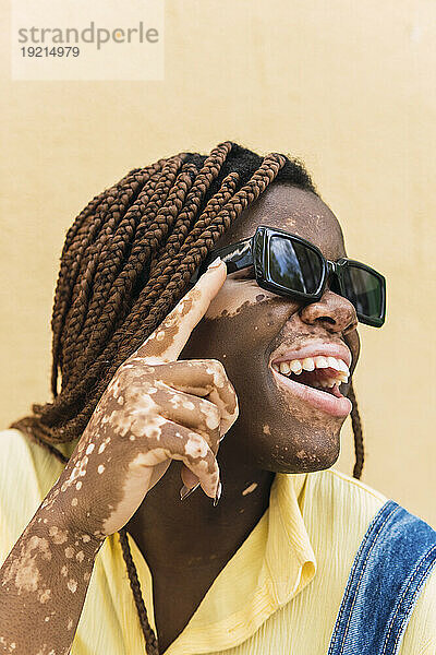Glückliche junge Frau mit Sonnenbrille vor einer pfirsichfarbenen Wand