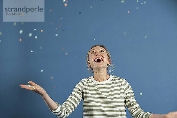 Glückliche Frau wirft Konfetti vor blauem Hintergrund