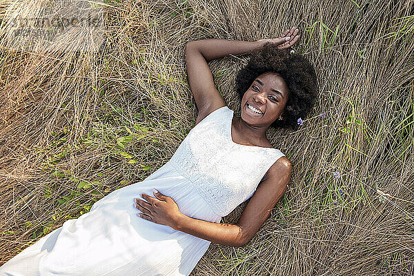 Happy young woman relaxing on dry grass in field