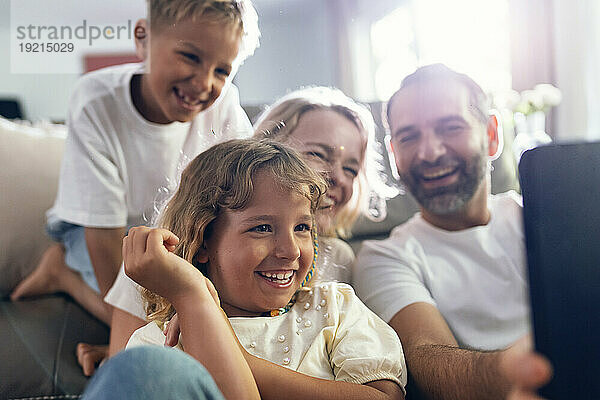 Lächelnder Mann  der zu Hause ein Selfie mit der Familie auf dem Handy macht