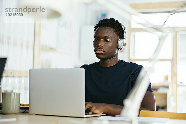 Junger Student mit kabellosen Kopfhörern und Laptop an der Universität