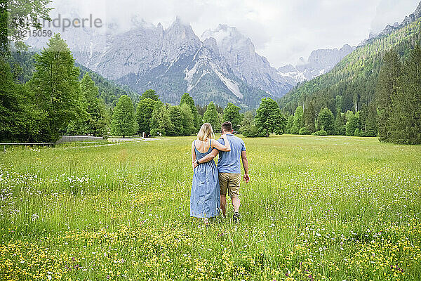 Man and woman walking together on grass in front of mountains