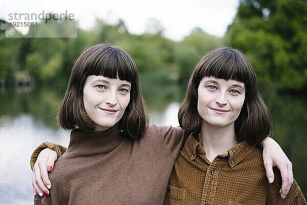 Smiling twin sisters with arms around near lake