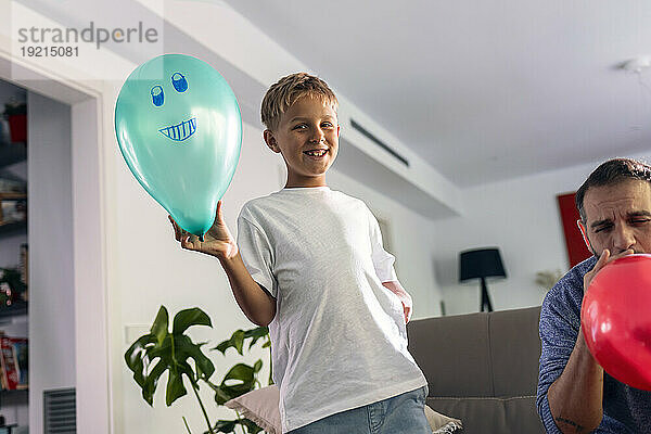 Lächelnder Junge mit Luftballon  der zu Hause neben dem Vater steht