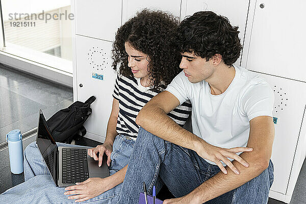 Lächelnde Studenten benutzen Laptop vor Schließfach an der Universität
