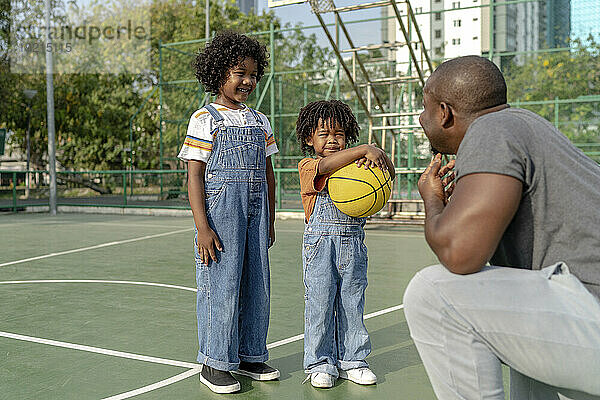 Lächelnde Kinder reden mit ihrem Vater auf dem Basketballplatz