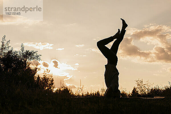 Silhouette einer Frau  die bei Sonnenuntergang Kopfstand-Yoga praktiziert