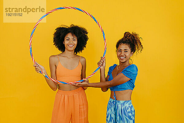 Lächelnde Frauen mit Plastikreifen vor gelbem Hintergrund
